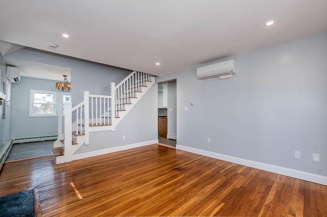 unfurnished living room featuring baseboards, stairway, an AC wall unit, and wood finished floors