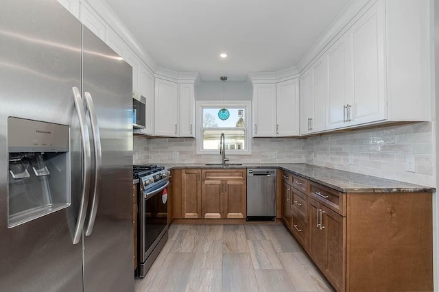 kitchen featuring white cabinets, decorative backsplash, dark stone countertops, stainless steel appliances, and a sink