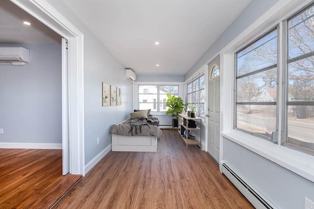 interior space with a baseboard heating unit, a wall mounted air conditioner, baseboards, and wood finished floors