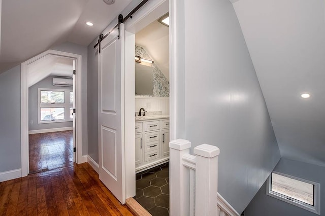 corridor featuring a barn door, baseboards, dark wood finished floors, vaulted ceiling, and a wall mounted AC