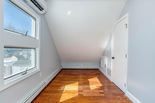 additional living space featuring a baseboard radiator, vaulted ceiling, wood finished floors, and an AC wall unit