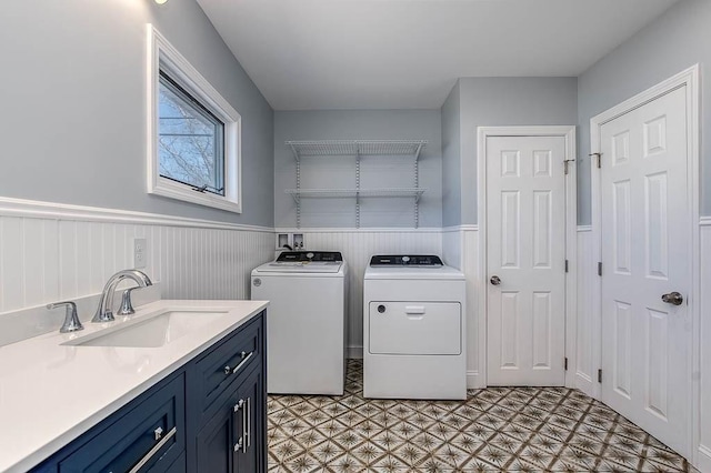 clothes washing area with cabinet space, wainscoting, a sink, and separate washer and dryer