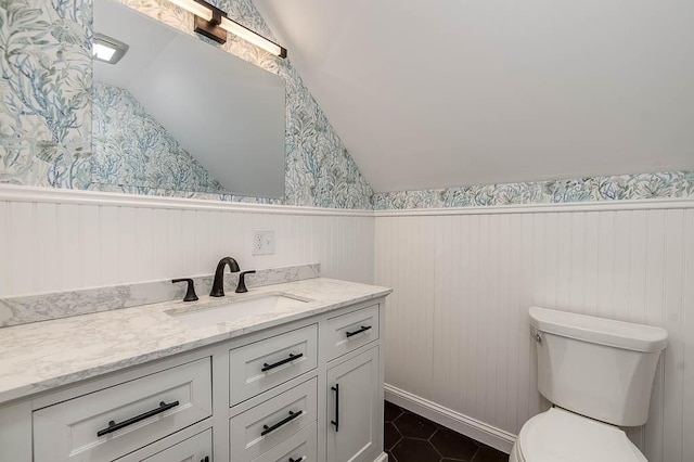 bathroom featuring lofted ceiling, wainscoting, vanity, and toilet