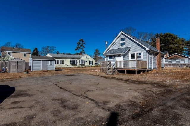 rear view of property featuring a shed, a chimney, an outbuilding, and a wooden deck