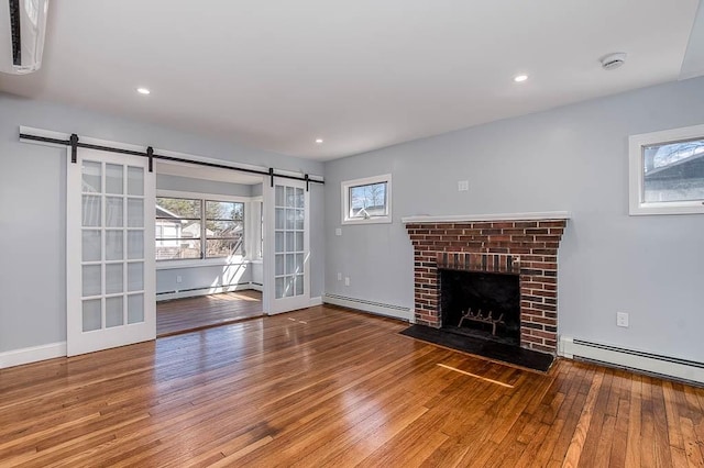 unfurnished living room with a barn door, baseboard heating, a baseboard radiator, and hardwood / wood-style flooring