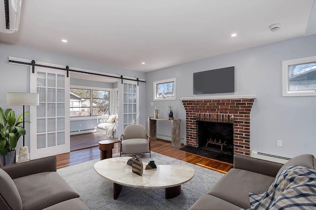 living room with a barn door, a baseboard radiator, wood finished floors, and a wealth of natural light