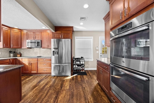 kitchen with light stone counters, backsplash, dark wood-type flooring, and stainless steel appliances