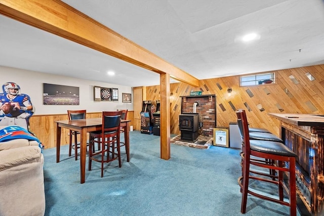 carpeted dining room with beam ceiling, indoor bar, a wood stove, and wooden walls