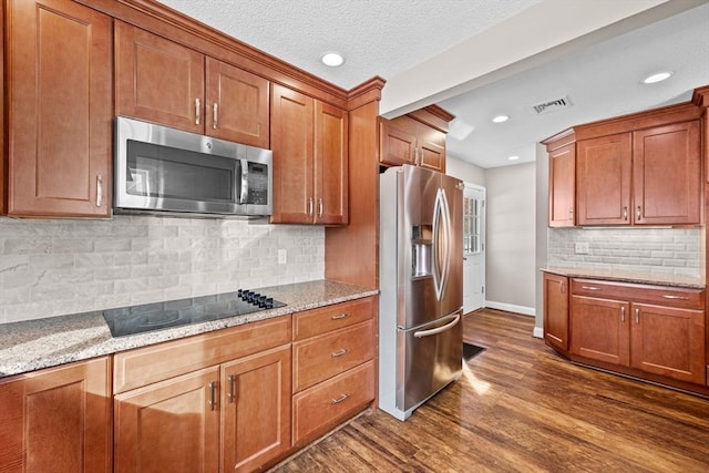 kitchen featuring appliances with stainless steel finishes, tasteful backsplash, light stone countertops, dark wood-type flooring, and a textured ceiling