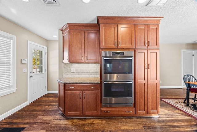 kitchen with light stone counters, a textured ceiling, dark hardwood / wood-style flooring, double oven, and decorative backsplash