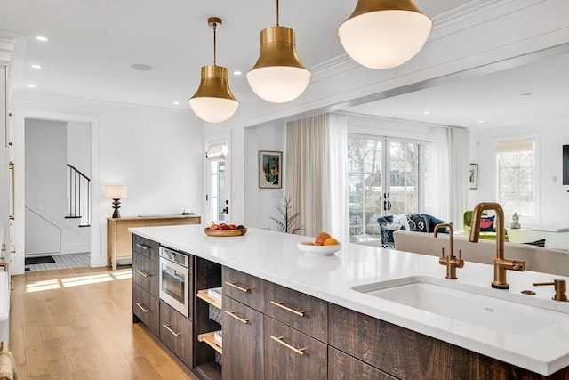 kitchen with modern cabinets, a sink, dark brown cabinetry, light wood finished floors, and light countertops