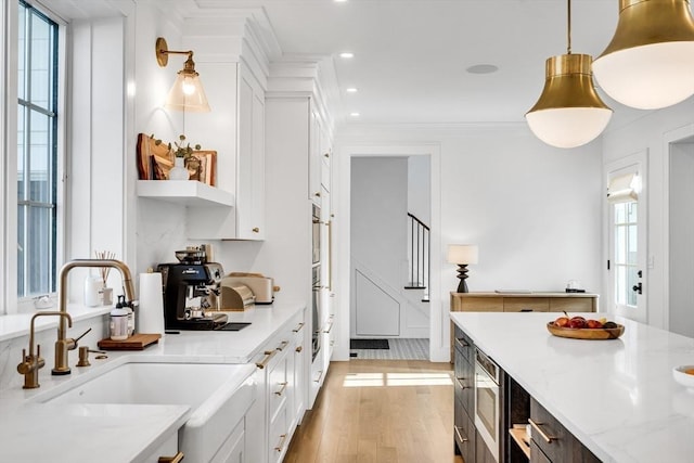 kitchen featuring a sink, light wood-style flooring, white cabinets, and ornamental molding