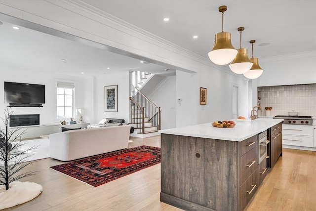 kitchen with light wood finished floors, an island with sink, ornamental molding, open floor plan, and backsplash