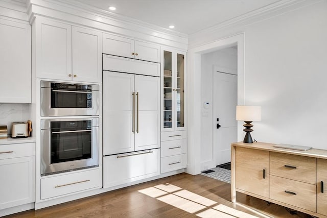 kitchen featuring glass insert cabinets, ornamental molding, wood finished floors, white cabinets, and paneled refrigerator