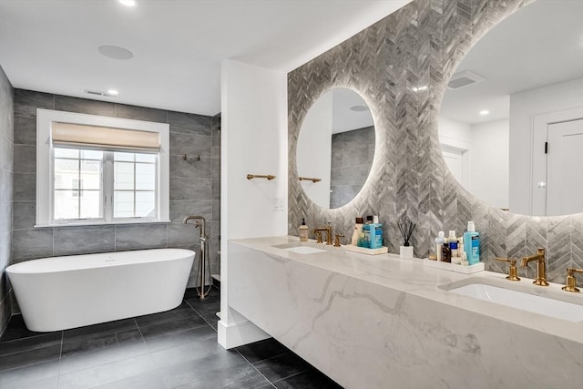 bathroom with tile patterned floors, a soaking tub, tile walls, and a sink