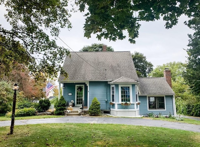 view of front of house featuring a chimney, a front yard, and roof with shingles