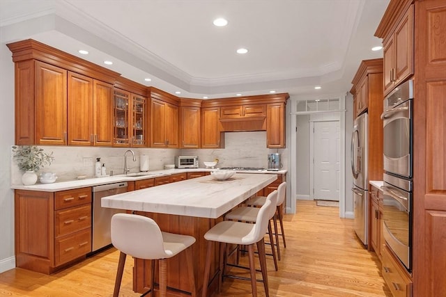 kitchen featuring appliances with stainless steel finishes, brown cabinetry, light countertops, recessed lighting, and a kitchen bar