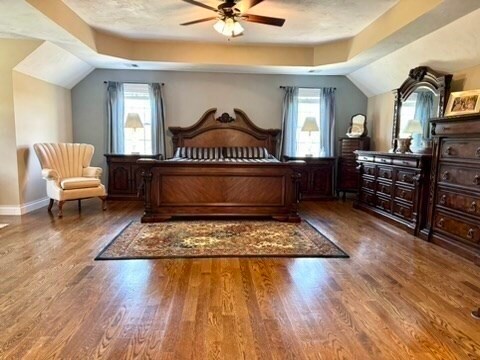 bedroom with vaulted ceiling, multiple windows, wood-type flooring, and ceiling fan