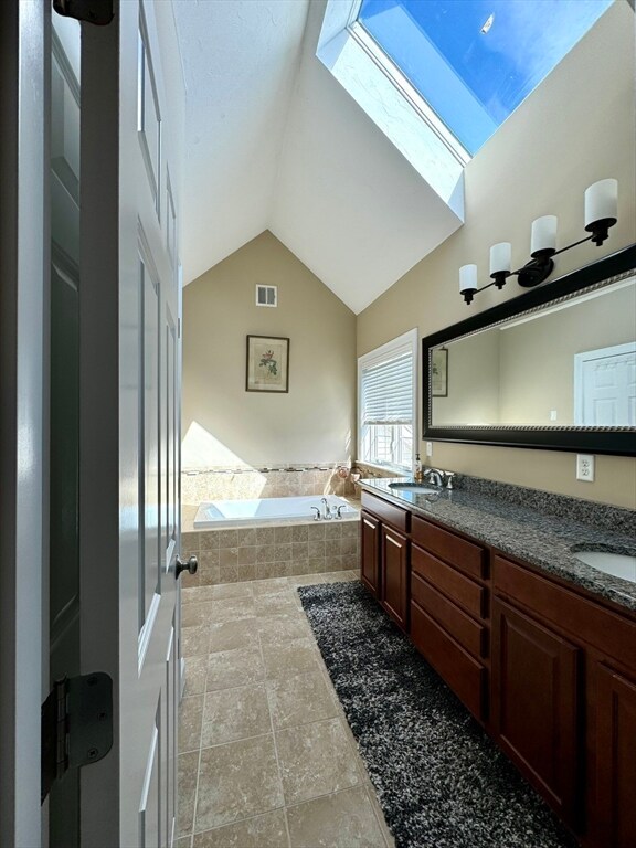 bathroom with vanity, lofted ceiling with skylight, and a relaxing tiled tub