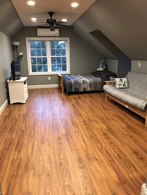 unfurnished bedroom with a wall mounted AC, wood-type flooring, ceiling fan, and vaulted ceiling