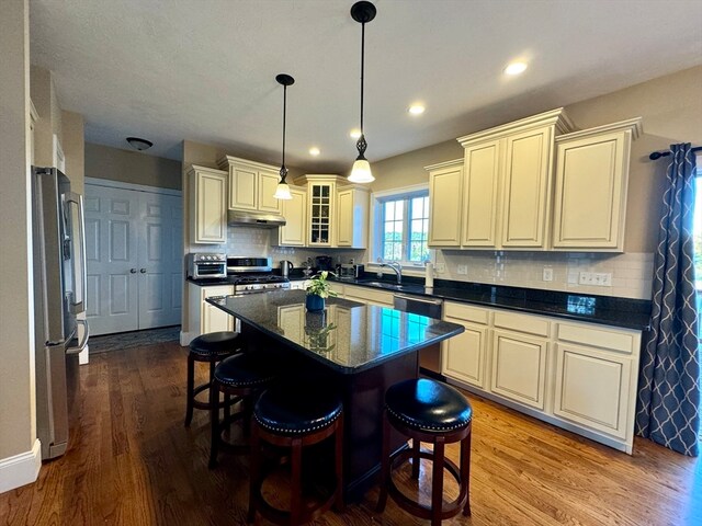 kitchen featuring decorative backsplash, a kitchen island, light hardwood / wood-style flooring, decorative light fixtures, and appliances with stainless steel finishes