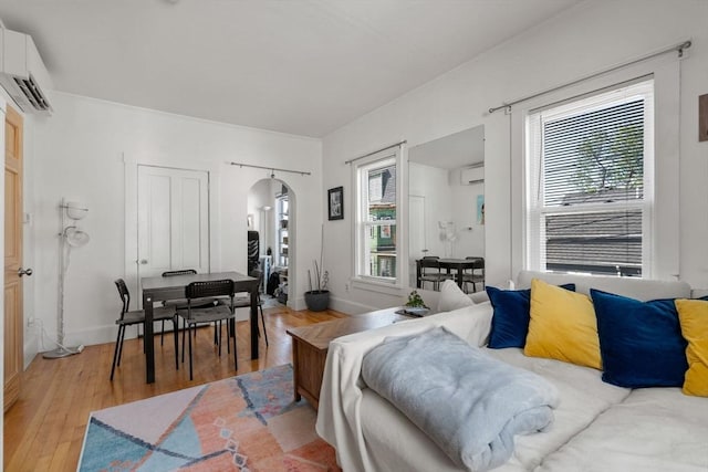 living area with arched walkways, light wood-style flooring, a wall mounted AC, and baseboards