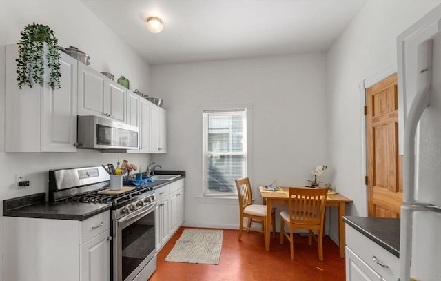 kitchen featuring appliances with stainless steel finishes, dark countertops, white cabinets, and a sink