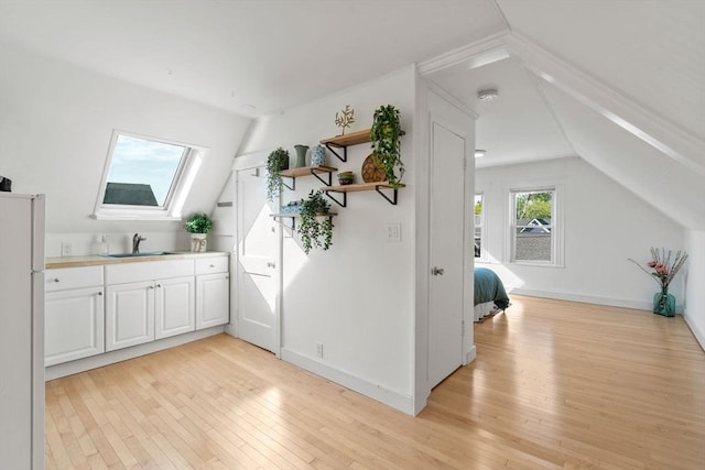 bar area featuring a sink, freestanding refrigerator, light wood finished floors, a skylight, and vaulted ceiling
