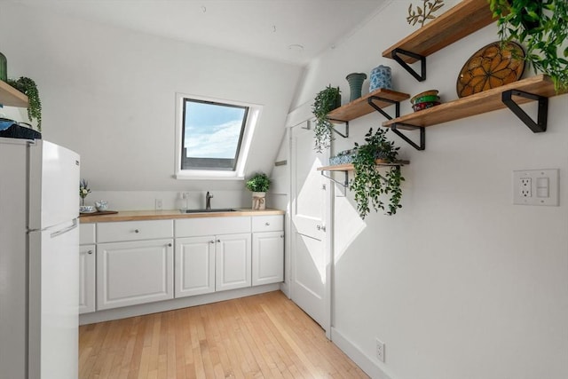 kitchen featuring open shelves, freestanding refrigerator, a sink, and white cabinetry