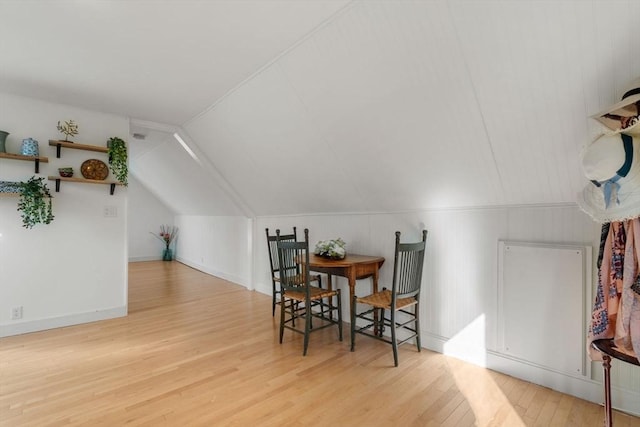 dining space featuring wood finished floors, lofted ceiling, and baseboards
