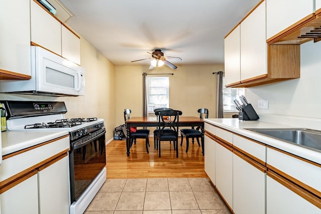 kitchen featuring white microwave, range with gas cooktop, ceiling fan, light countertops, and white cabinetry