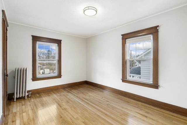 spare room with crown molding, radiator heating unit, and light wood-type flooring