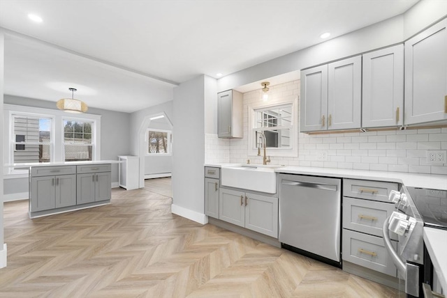 kitchen with sink, gray cabinets, appliances with stainless steel finishes, tasteful backsplash, and light parquet flooring