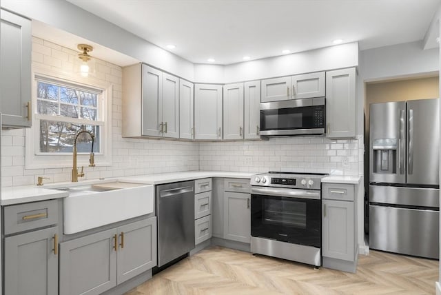 kitchen with gray cabinetry, sink, stainless steel appliances, and light parquet flooring