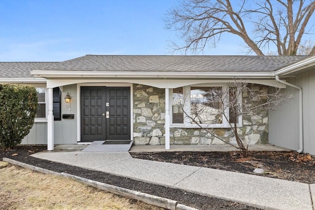 entrance to property with covered porch, stone siding, and roof with shingles