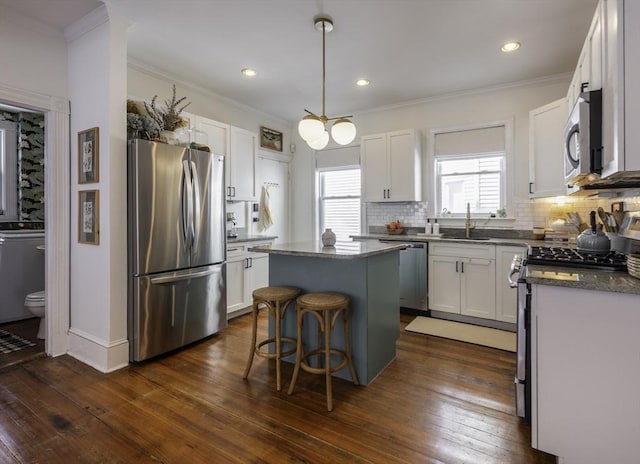kitchen featuring appliances with stainless steel finishes, a sink, a center island, tasteful backsplash, and white cabinetry