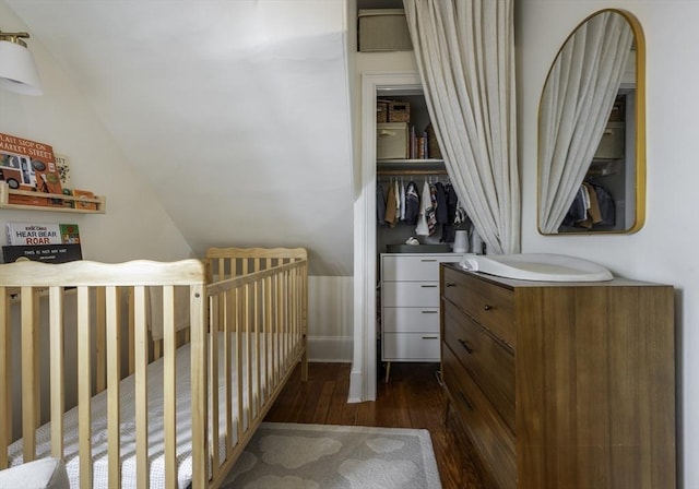 bedroom featuring dark wood-style flooring, vaulted ceiling, and a nursery area