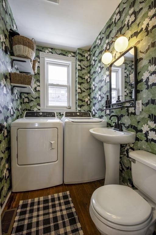 half bathroom with wallpapered walls, washing machine and clothes dryer, toilet, and wood finished floors