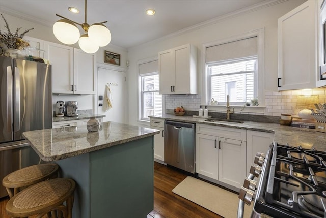 kitchen with appliances with stainless steel finishes, a sink, crown molding, white cabinets, and a breakfast bar