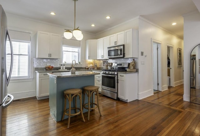 kitchen featuring appliances with stainless steel finishes, a kitchen island, decorative backsplash, white cabinets, and crown molding