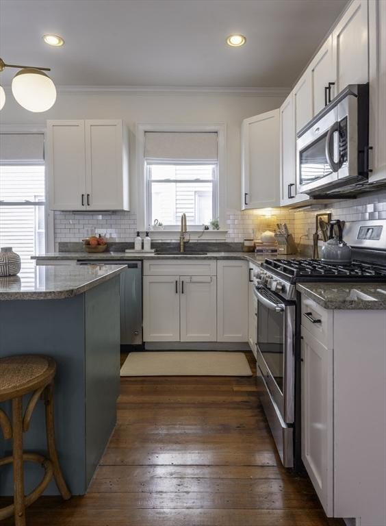 kitchen featuring stainless steel appliances, a sink, crown molding, white cabinets, and backsplash