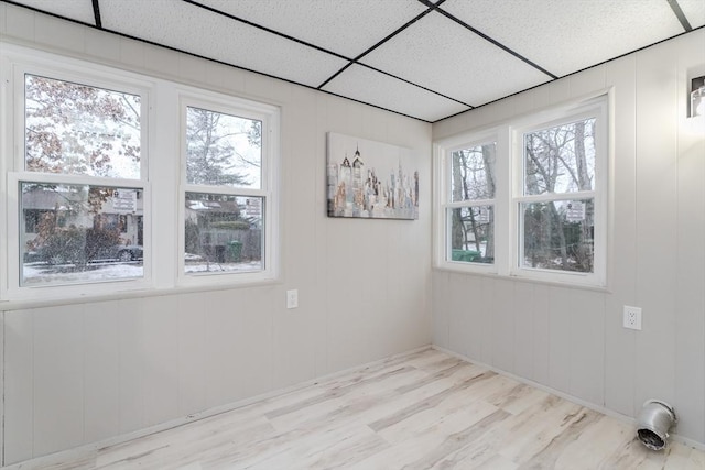 unfurnished room featuring plenty of natural light, a drop ceiling, and light wood-type flooring