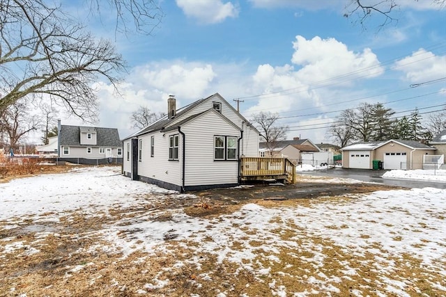 view of snow covered exterior featuring an outbuilding, a garage, and a deck