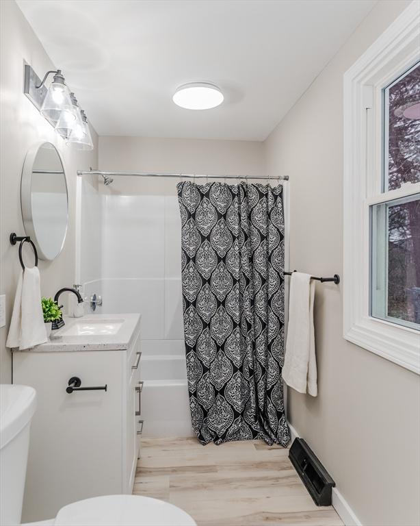 full bathroom with wood-type flooring, vanity, shower / bath combo with shower curtain, and toilet