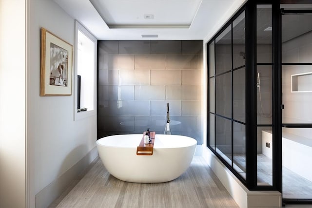 bathroom featuring a bathtub, tile walls, and a tray ceiling