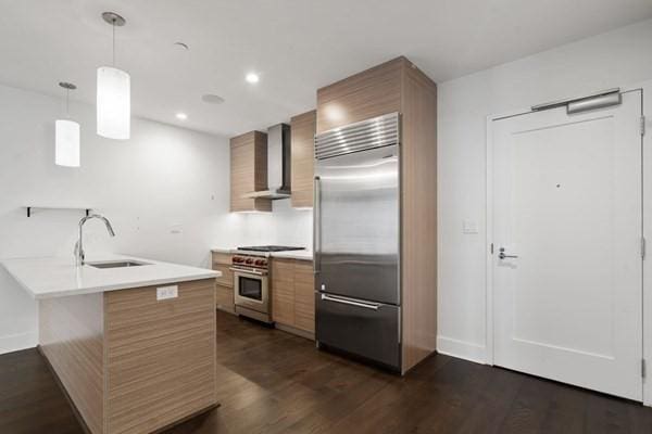 kitchen featuring wall chimney exhaust hood, premium appliances, dark wood-type flooring, sink, and decorative light fixtures