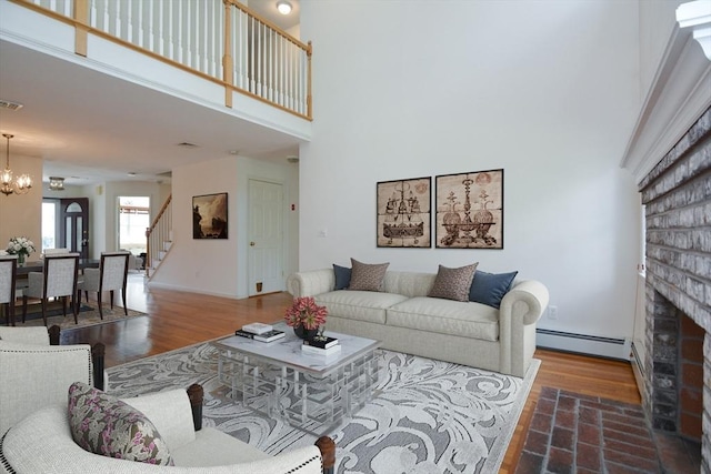 living area with an inviting chandelier, a brick fireplace, a towering ceiling, stairway, and a baseboard radiator
