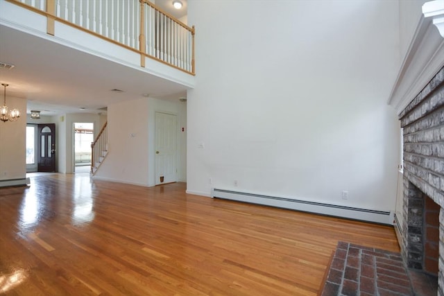 unfurnished living room with a brick fireplace, a chandelier, stairs, wood finished floors, and a baseboard radiator