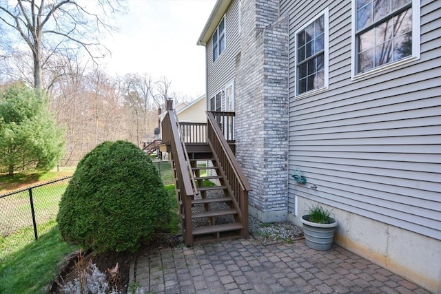 view of side of home with fence, brick siding, a deck, stairway, and a patio area