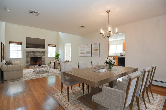 dining area with an inviting chandelier, a brick fireplace, light wood-type flooring, and visible vents